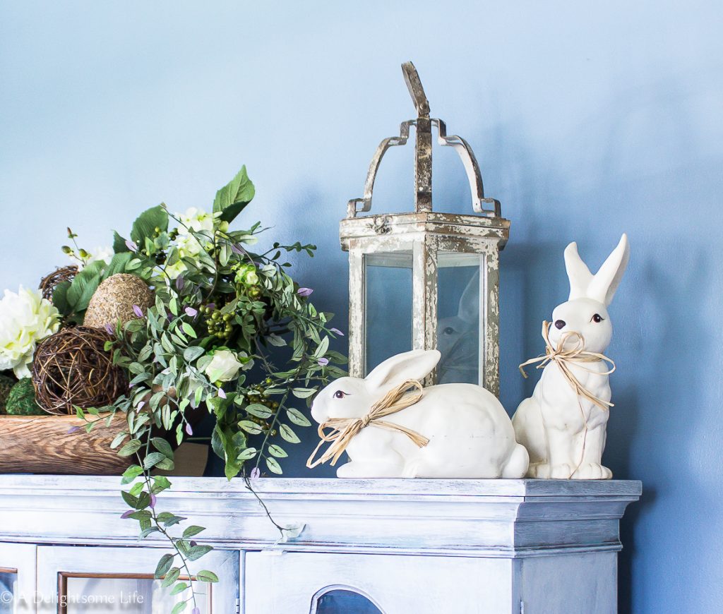 Spring Home Tour rabbits, Lavender and greenery on top of the dining room china hutch on A Delightsome Life #springdecor #easterdecor #breaddoughbowl #easterrabbits #diningroomdecor #blue