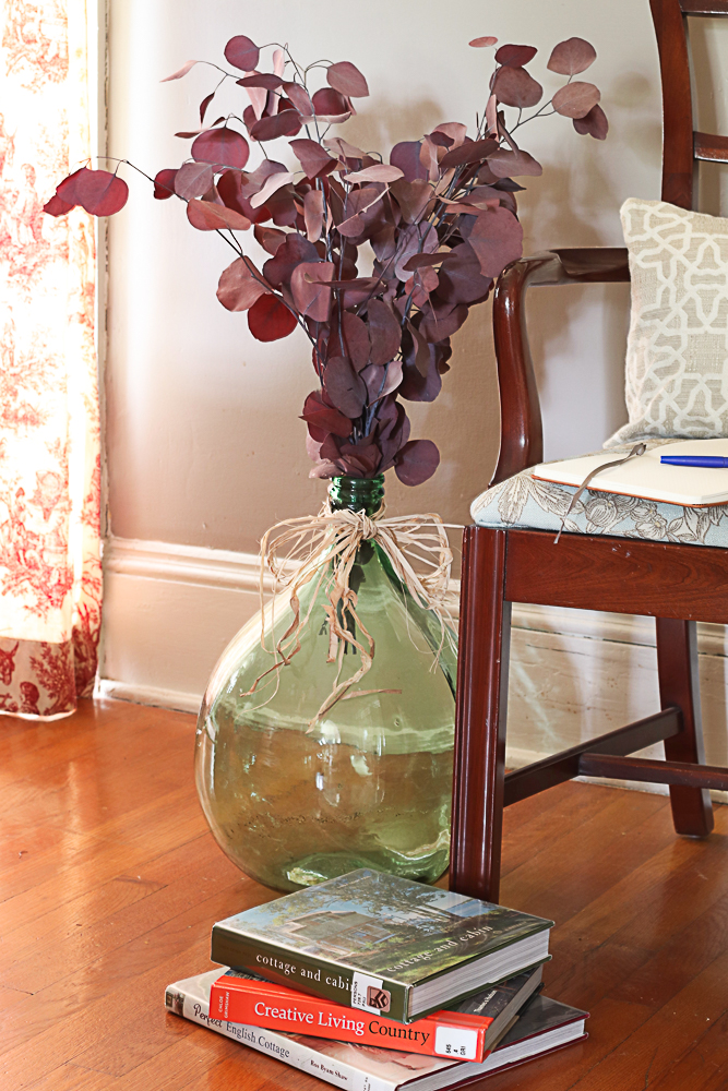 dried Eucalyptus in demijohn by chair and books